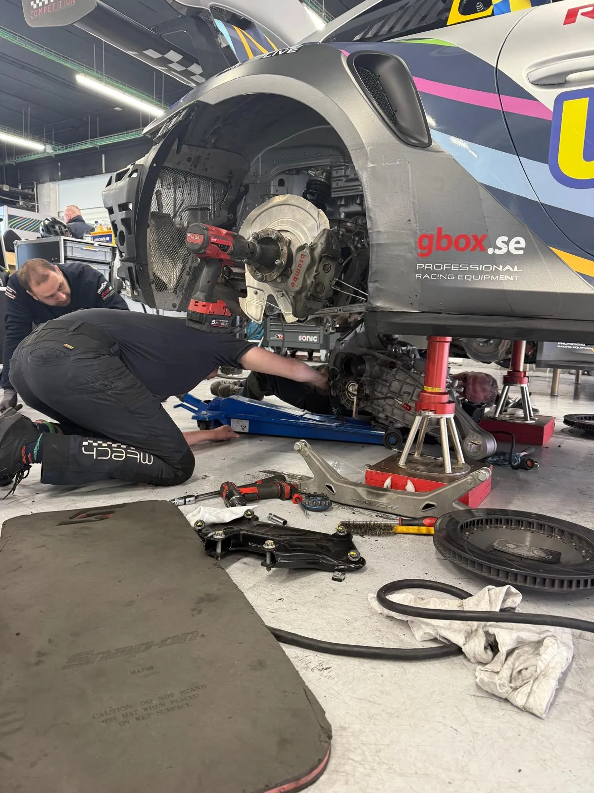 A front corner stripped on stands, brake disc and suspension components laid out on the floor beside it