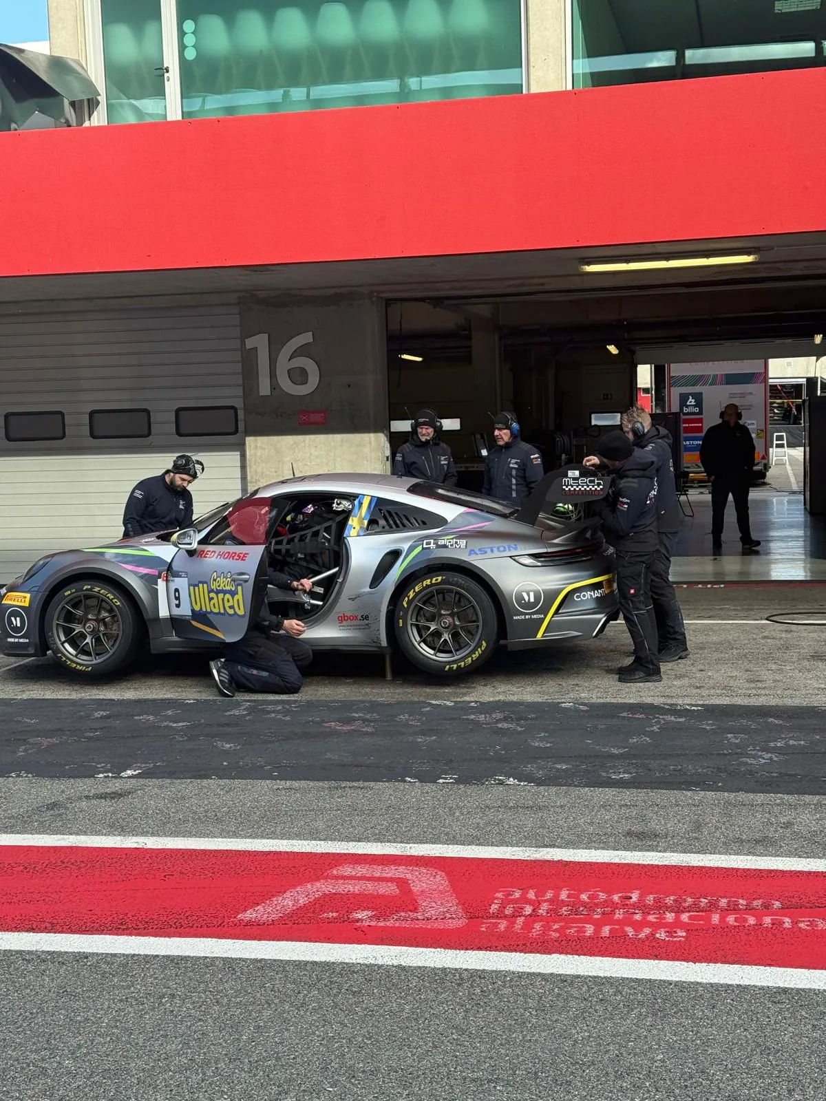 The car in its pit box with mechanics working around it, garage door up onto the pit lane